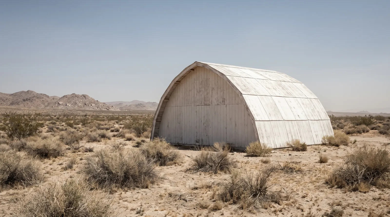 A large white domed timber building standing alone in flat open Mojave desert scrub under a pale sky