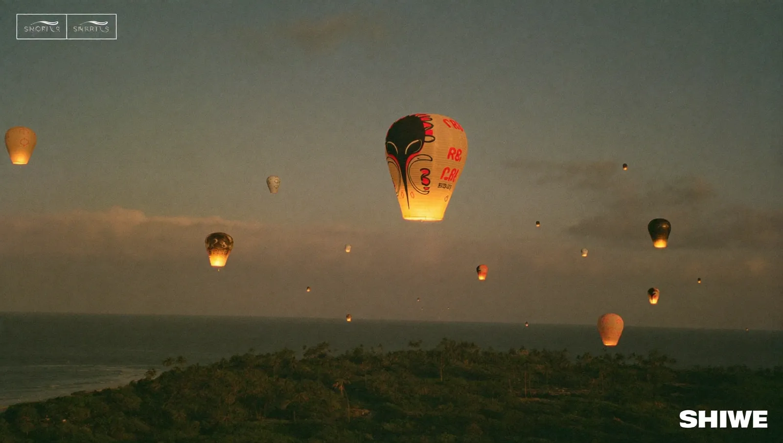 Paper hot-air sky lanterns rising into a warm tropical night sky above palm trees and a dark Caribbean coastline