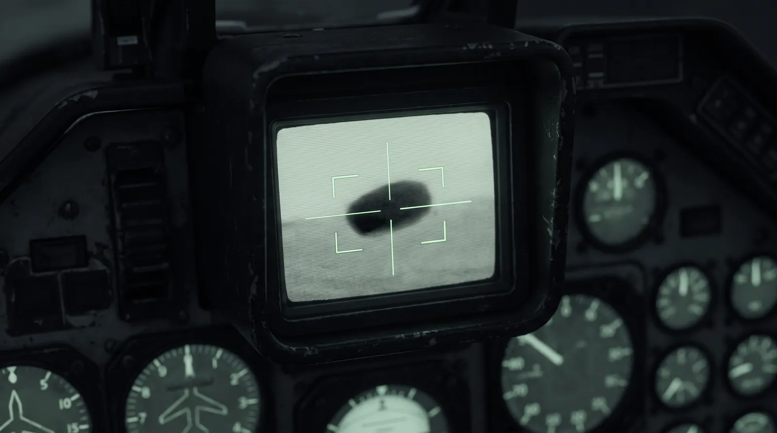 A military infrared targeting display in a dark cockpit showing a featureless dark oval against a grainy pale sky, framed by sensor crosshairs