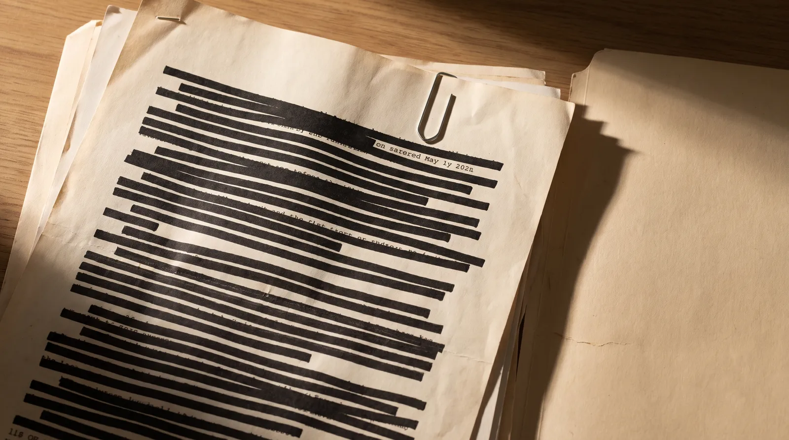 Loose printed documents spread on a desk, several pages heavily censored with thick black redaction bars across most of their lines