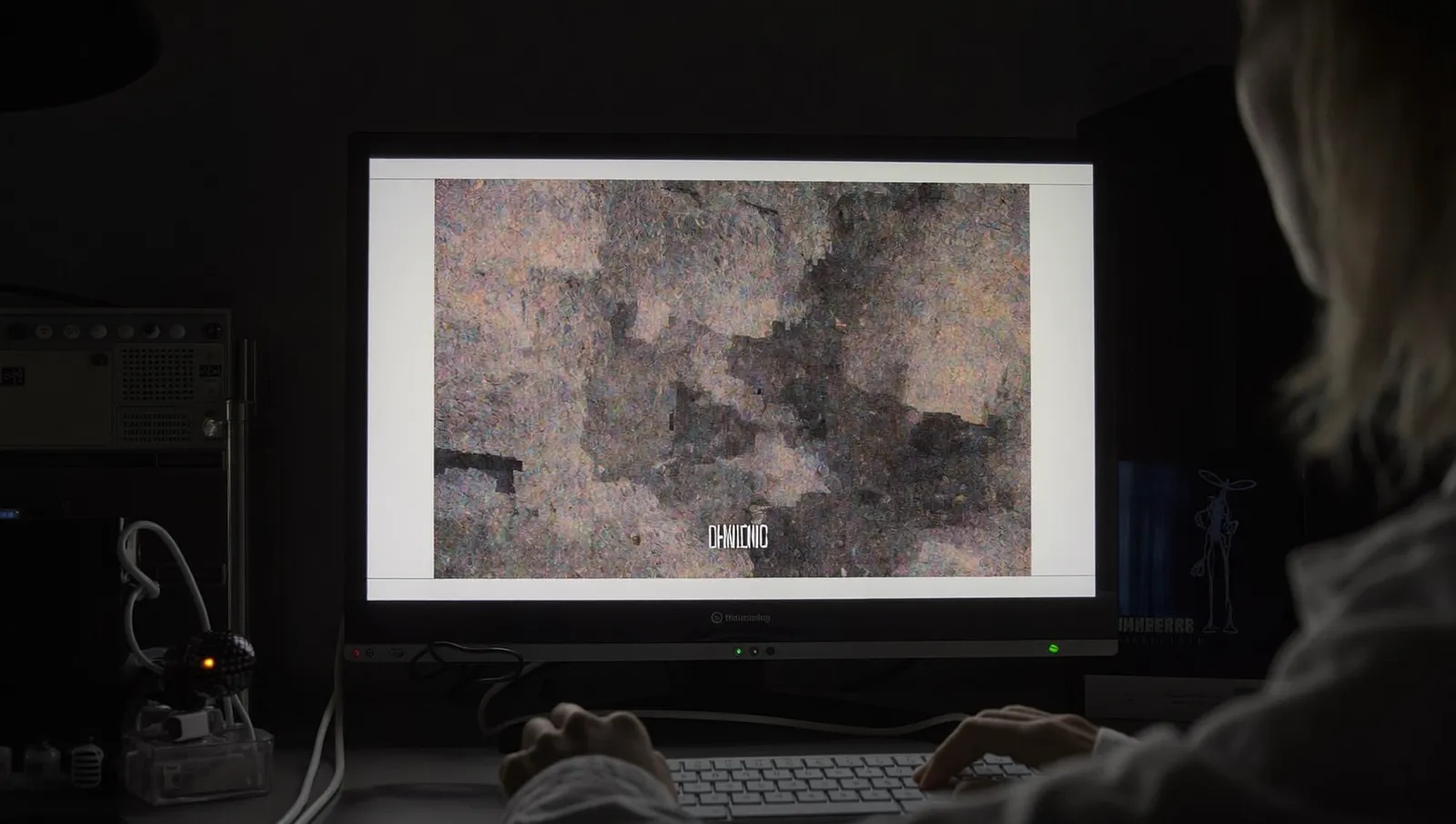 An analyst at a darkened workstation studying a heavily magnified grainy monochrome frame on a large monitor