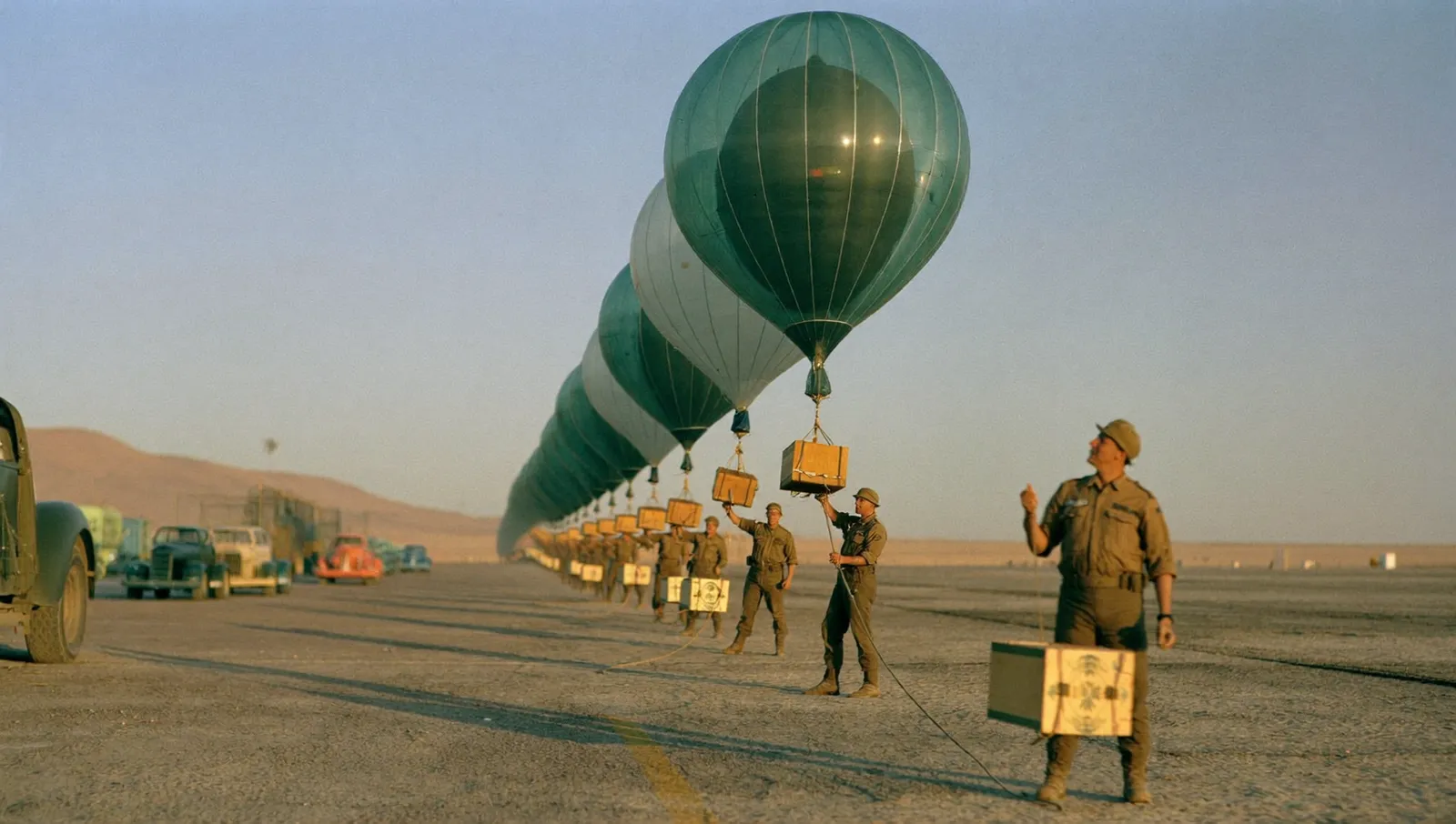 Nineteen-forties technicians on a desert airfield at dawn releasing a long train of small research balloons carrying instrument packages