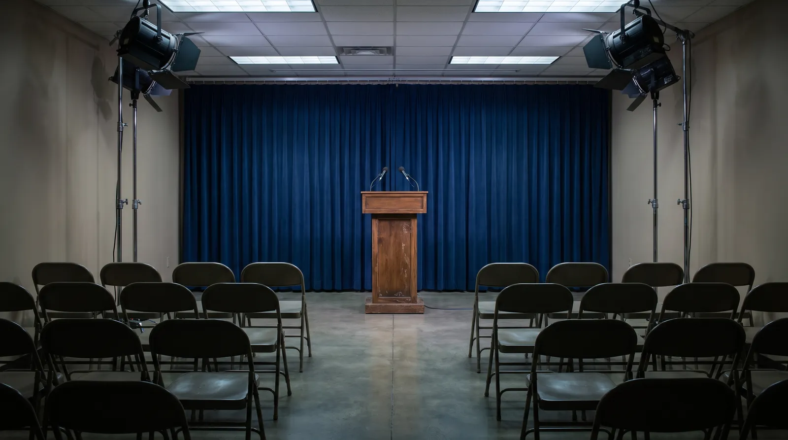 An empty government press briefing room with a plain lectern, two microphones and rows of unoccupied chairs