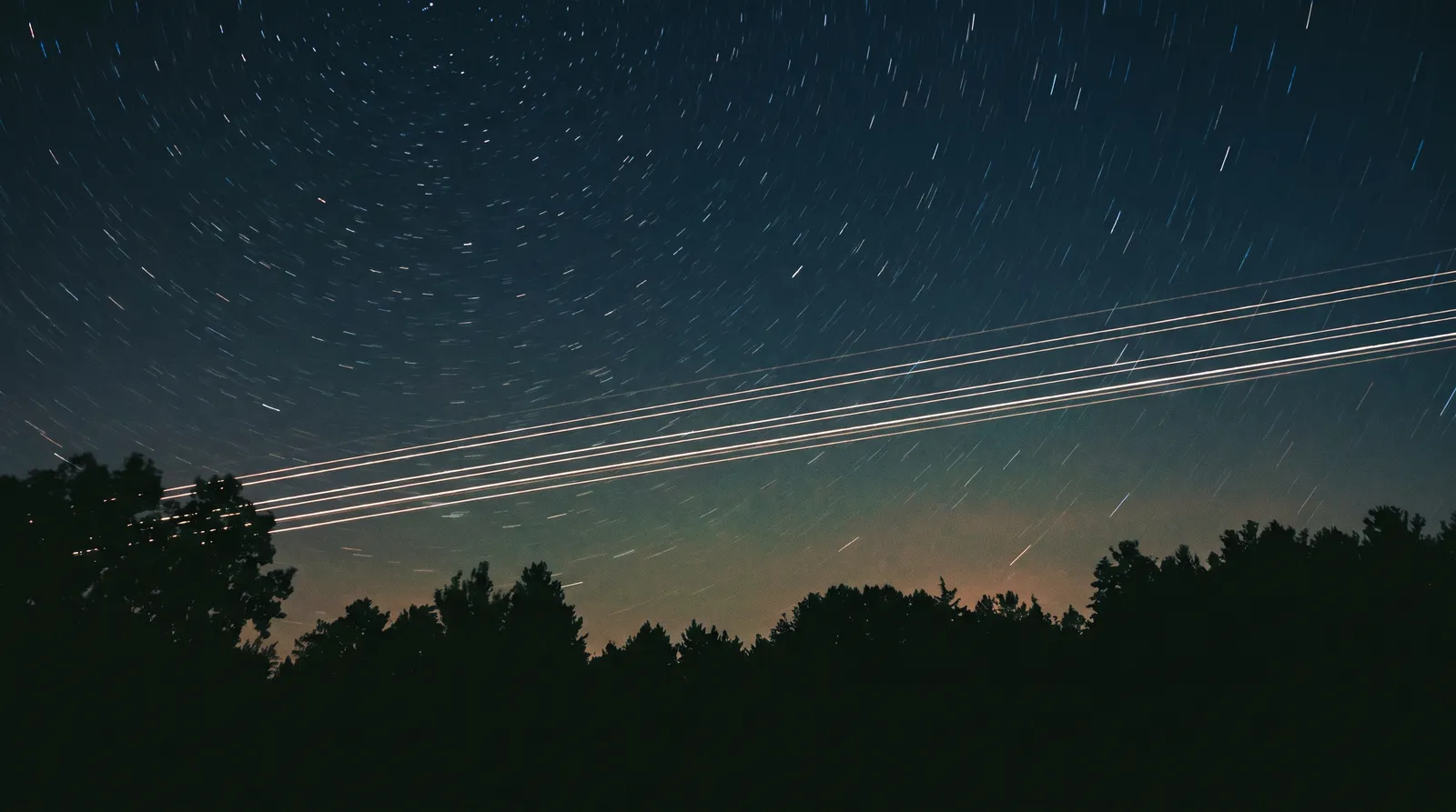 A long-exposure night photograph showing an evenly spaced train of bright satellite streaks marching in a straight line across a star field