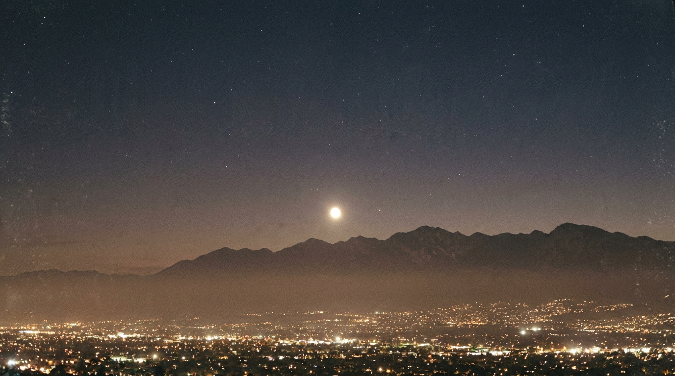 An extremely bright planet blazing low over a dark mountainous horizon beyond distant city lights
