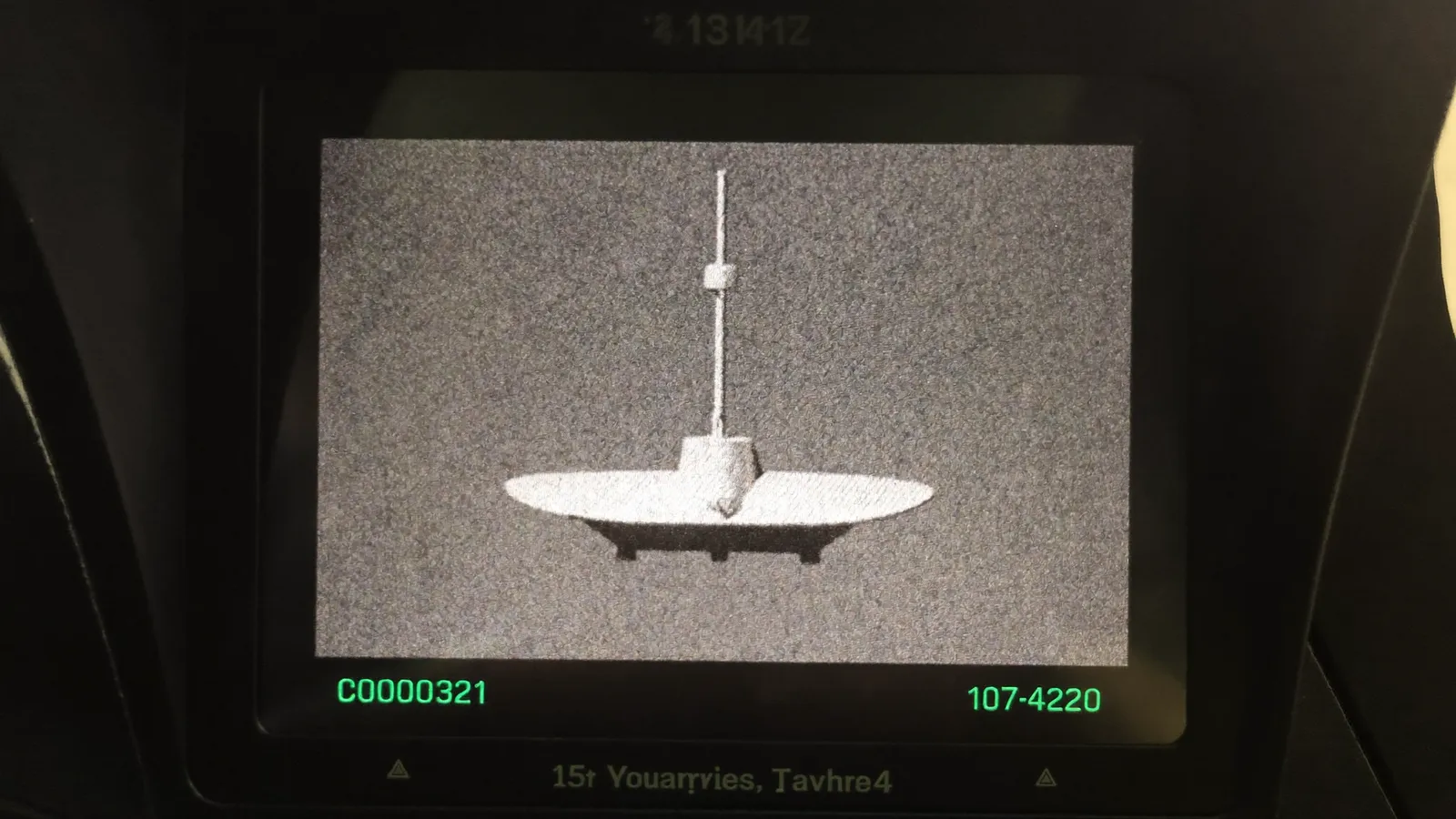 A military cockpit multifunction display showing a grainy monochrome infrared image of a small featureless oblong object against a grey sky