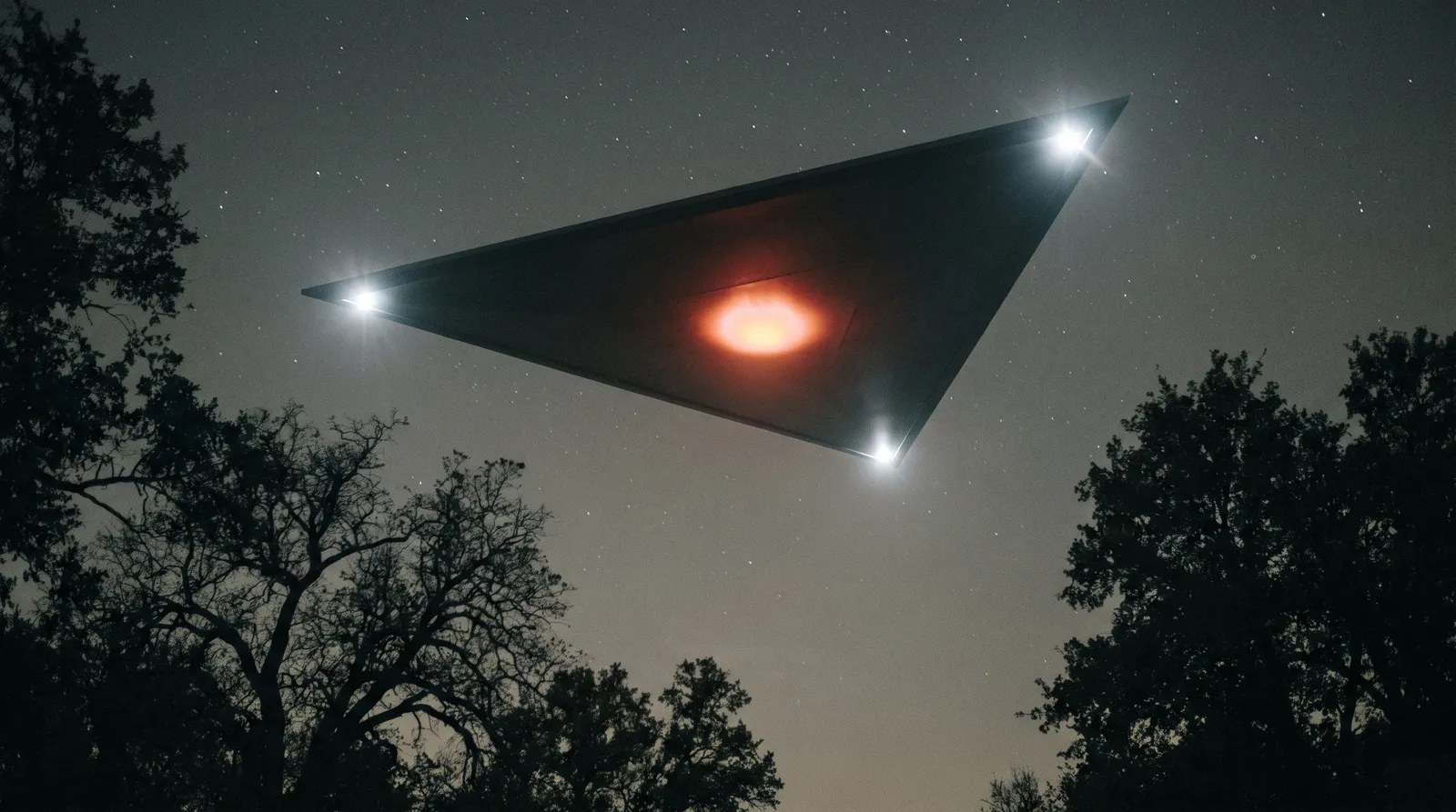 Looking up at the underside of a huge matte-black equilateral triangle at night, three white corner lights and a red-amber light at the centre