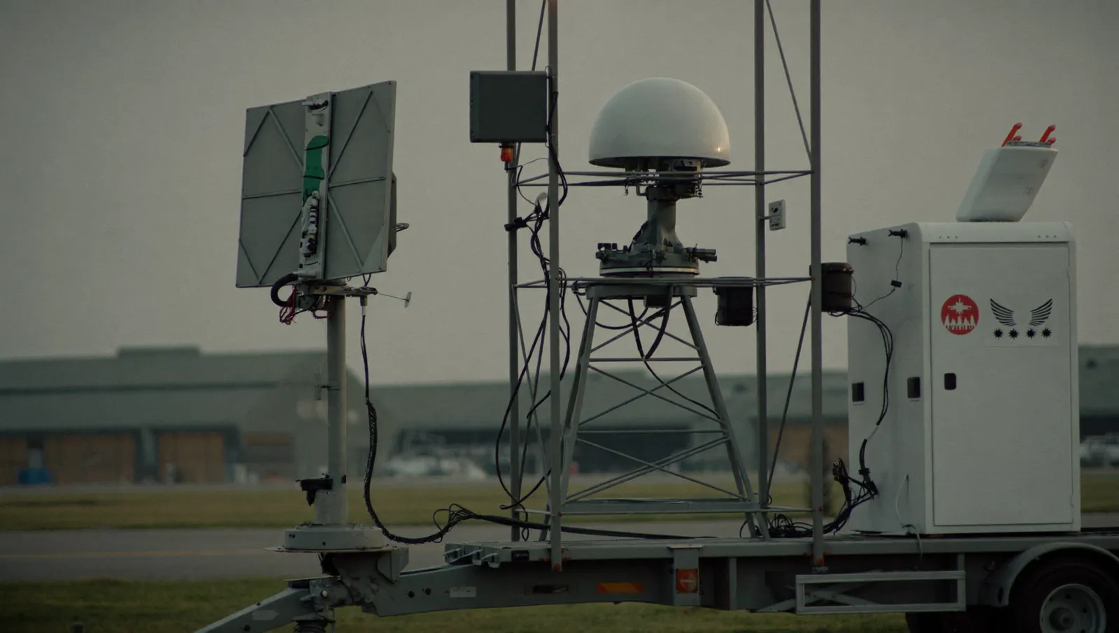 A trailer-mounted counter-drone radar and radio-frequency sensor mast standing on a military airbase flightline