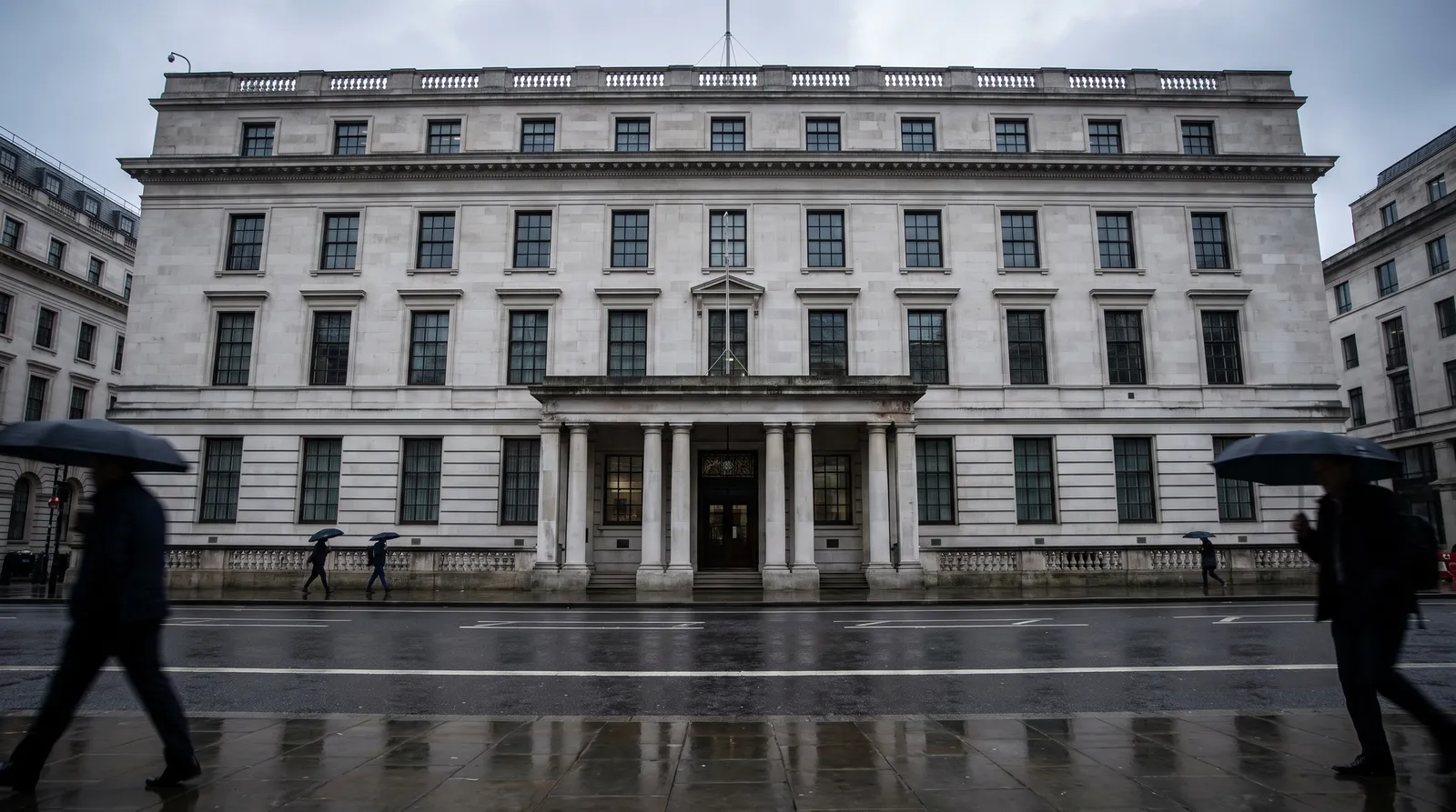 An imposing grey Portland stone government ministry building in London seen from across a wet street on an overcast day